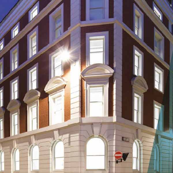 A red-brick building, pictured at night with traditional white sash windows illuminated from within.