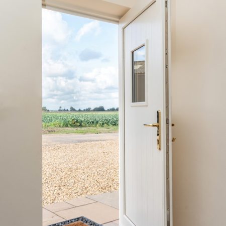 cream entrance door with small glass vision panel window and gold hardware. Secured by design with multipoint locking.